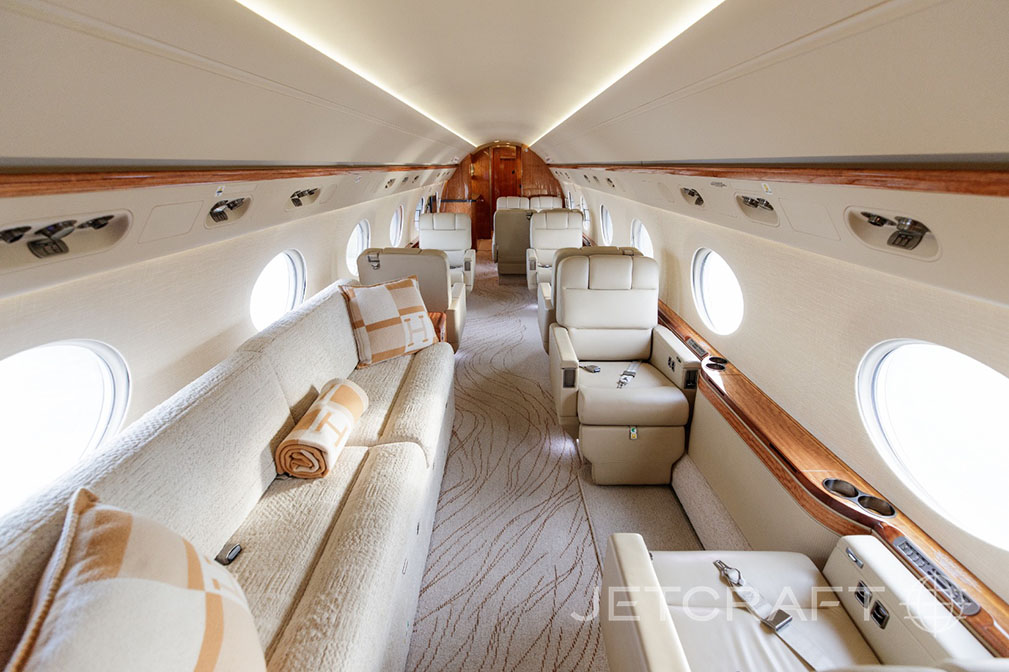 The aft cabin of a business jet, featuring a long cream sofa with pillows and individual seats.