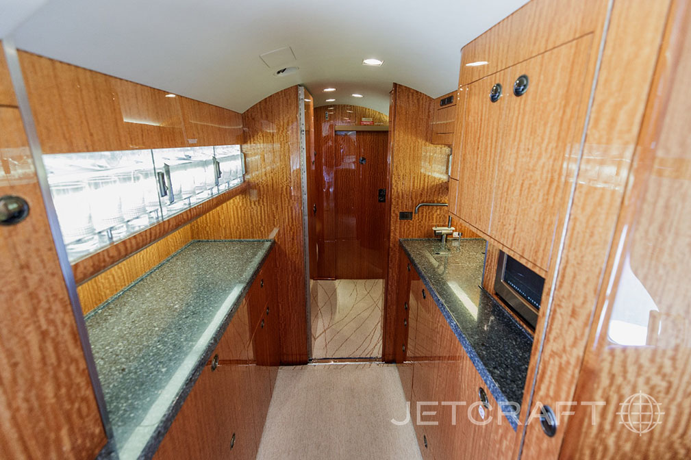 The galley area of a business jet, featuring dark granite countertops and polished wood cabinetry.